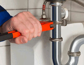 Technician using a wrench to tighten a chrome sink P-trap under a sink