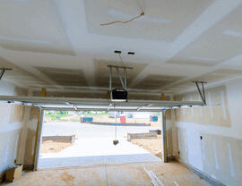 Unfinished garage interior with taped drywall, open garage door, and ceiling-mounted opener.