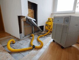 Yellow hoses and dehumidifier drying a water-damaged floor and wall