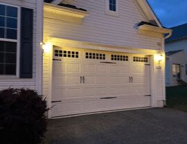 White garage door and siding at dusk with exterior lights on