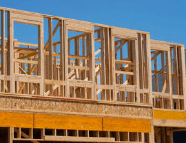 Multi-story wood frame construction on a new home addition under a clear blue sky.