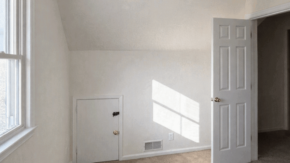 Small attic bedroom with sloped ceiling, beige carpet and a low storage door.