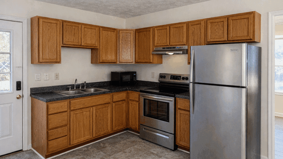 L-shaped kitchen with oak cabinets, black countertops, stainless stove and refrigerator.