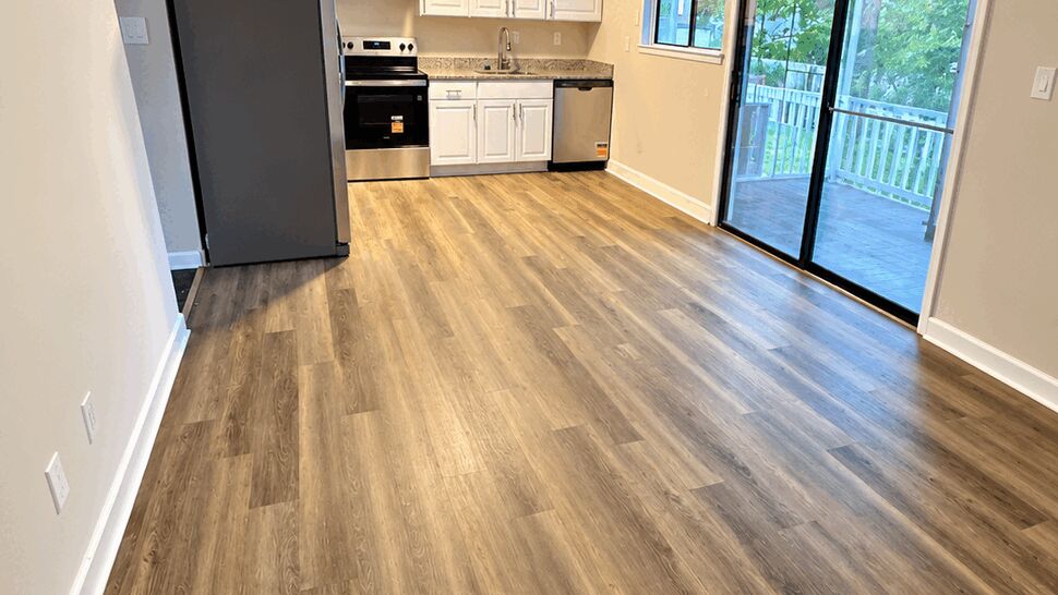 Bright Kitchen and Flooring Remodel | TSP Contracting Bright remodeled kitchen with white cabinets, stainless appliances, wood-look flooring, and a sliding glass door.