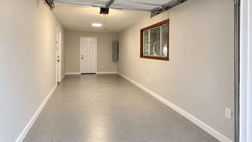 Finished garage with a speckled floor, painted walls, overhead door, and ceiling light.