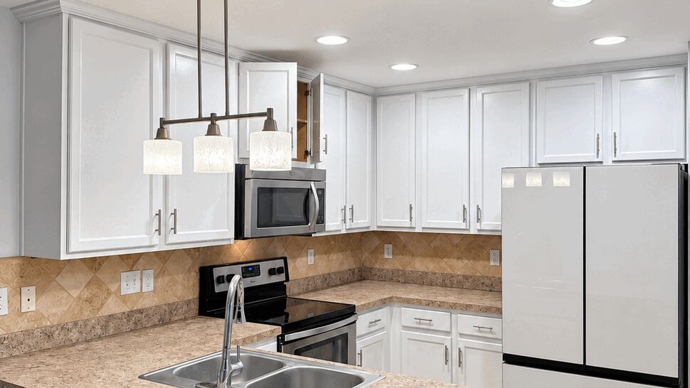Kitchen Peninsula and Cabinetry | TSP Contracting White-cabinet kitchen with peninsula sink, pendant lighting, appliances, and tile flooring