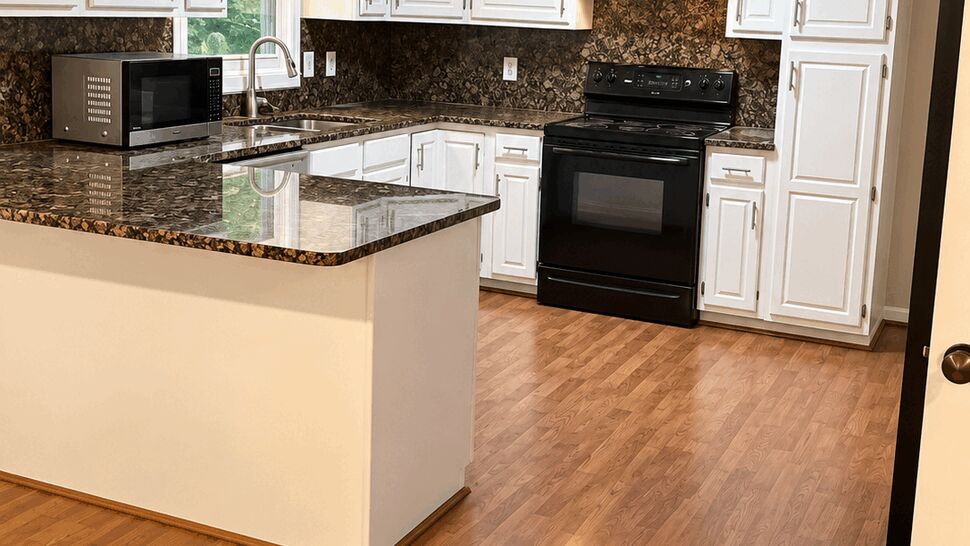 Renovated kitchen with white cabinets, dark countertops, black appliances, and wood flooring