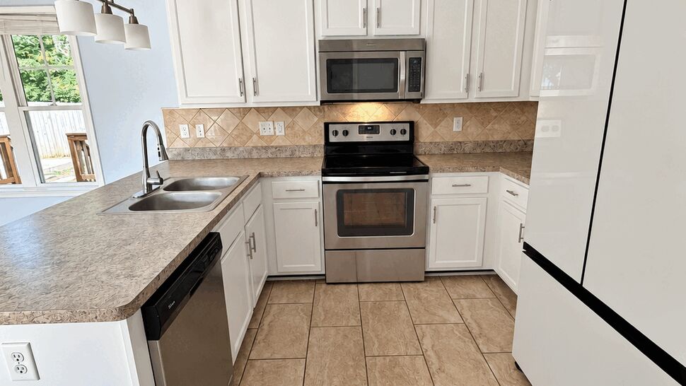 Bright kitchen with white cabinets, stainless steel appliances, tiled backsplash, and peninsula sink