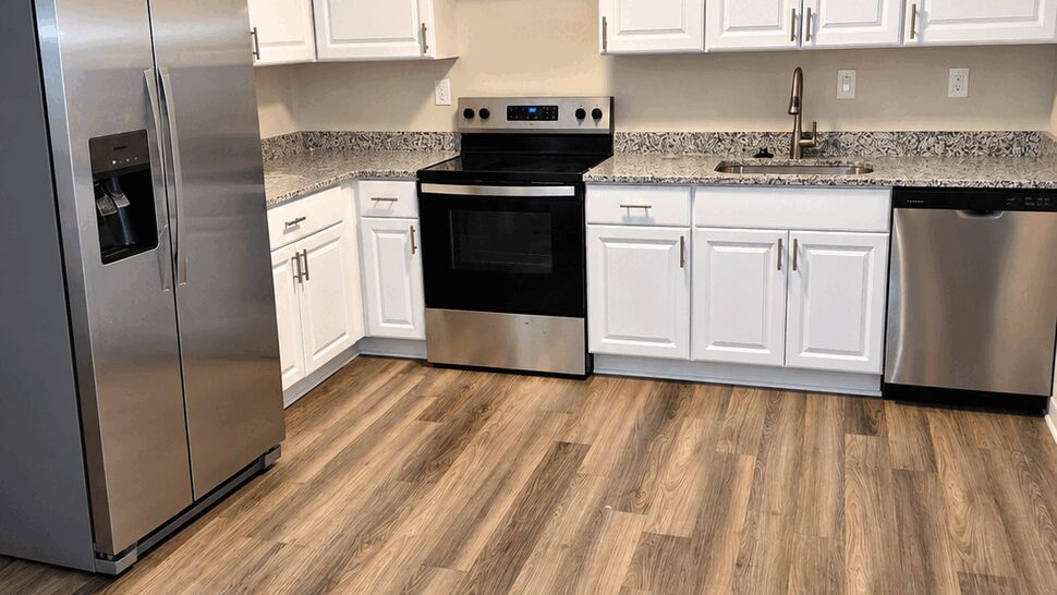 White Cabinet Kitchen Renovation | TSP Contracting Updated kitchen with white cabinets, stone counters, stainless appliances, sink, faucet, and wood-look flooring.