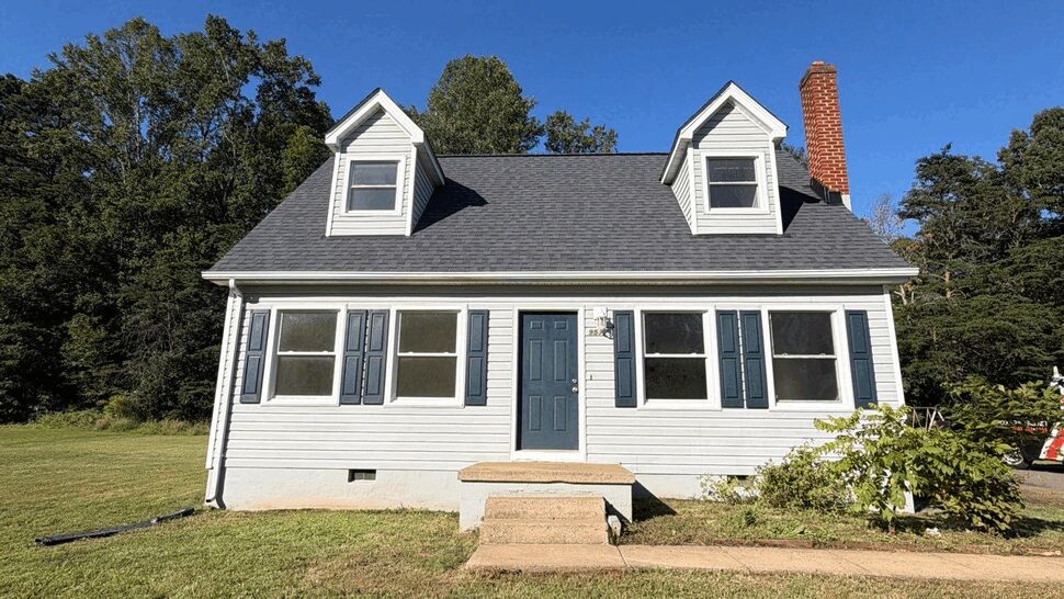 Front view of a white Cape-style house with blue door, dormers, and new looking siding.