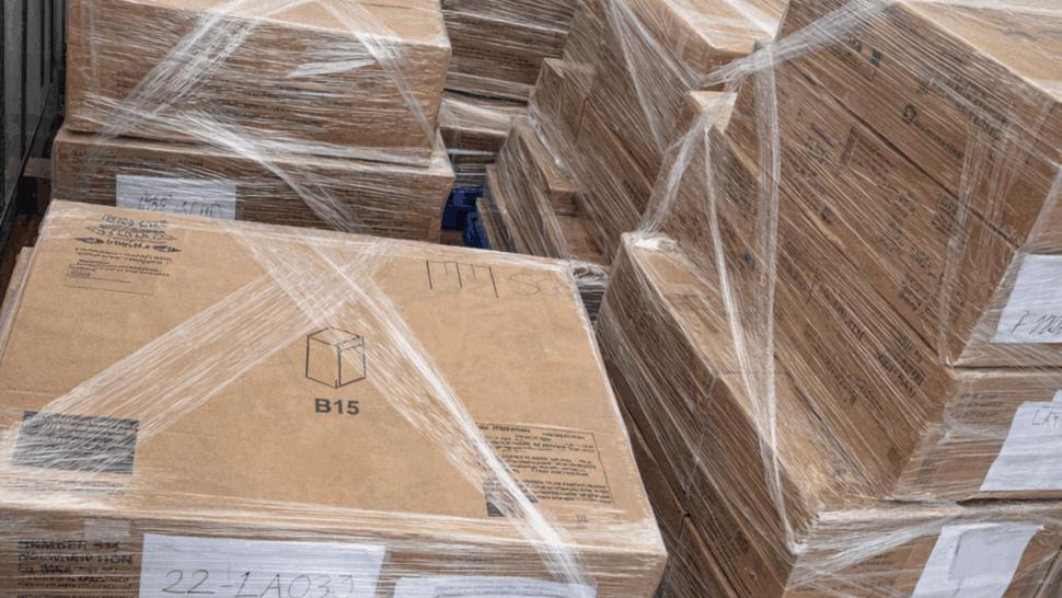 Shrink-wrapped cardboard boxes stacked on blue pallets inside a truck.
