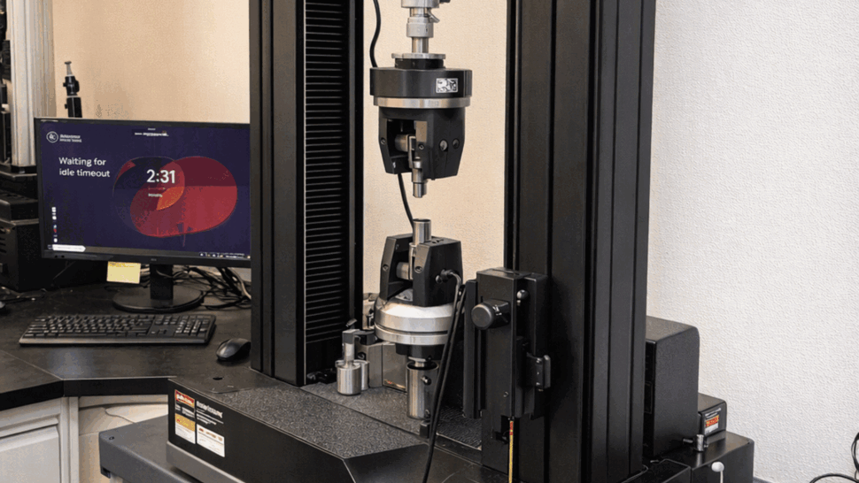 Instron tensile testing machine mounted on a lab workstation and desk