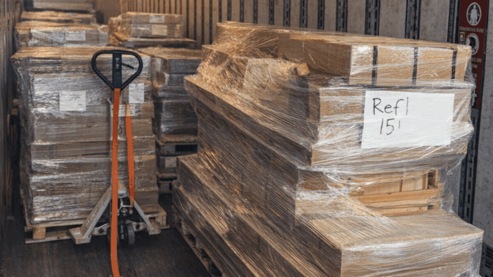 Pallet jack next to shrink-wrapped pallets inside a moving truck.
