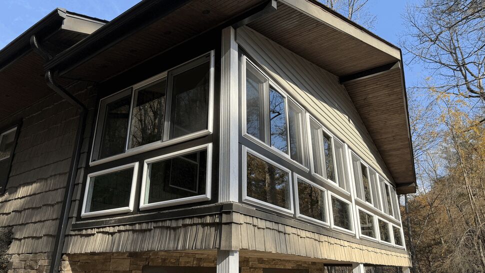 Corner sunroom enclosure with multiple white-framed windows on the upper level of a house