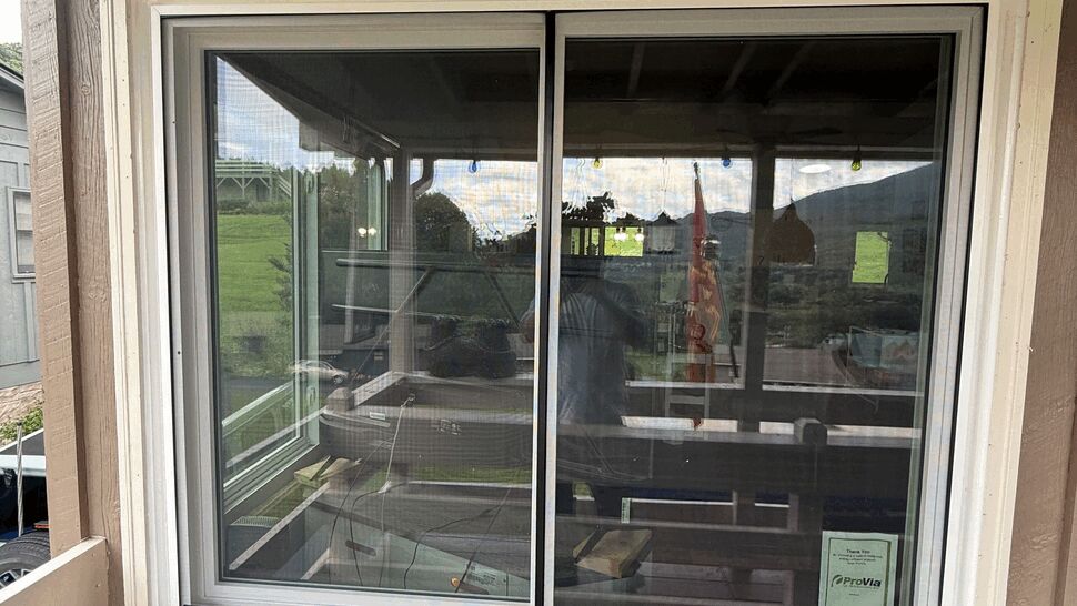 Exterior sliding window looking into a covered porch with screen and white trim.