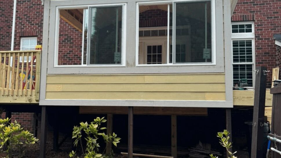 Exterior view of a raised sunroom with large windows and yellow siding on a brick house