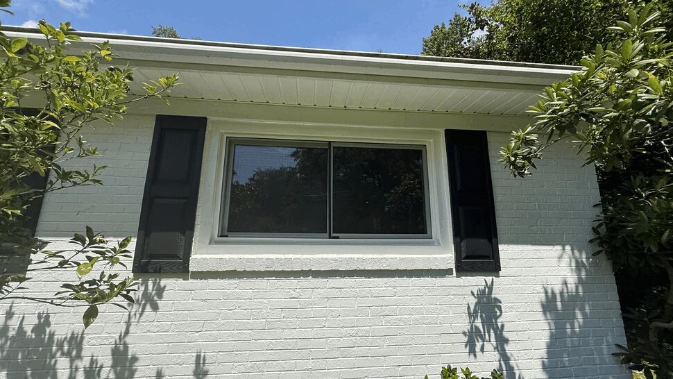 Wide exterior sliding window with black shutters on white brick wall