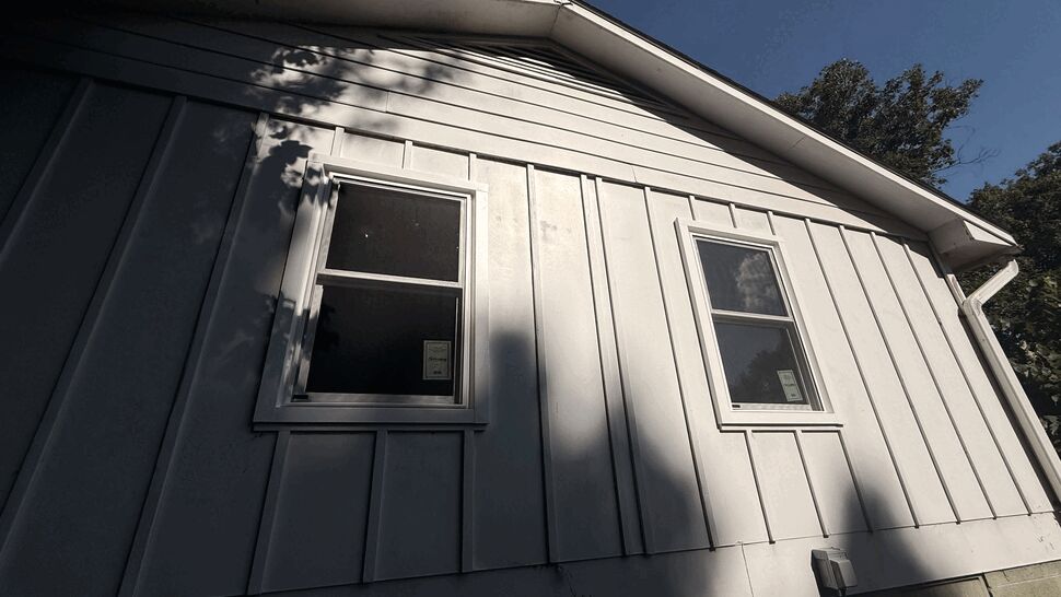 Gable end of house with two white-framed windows on vertical siding.