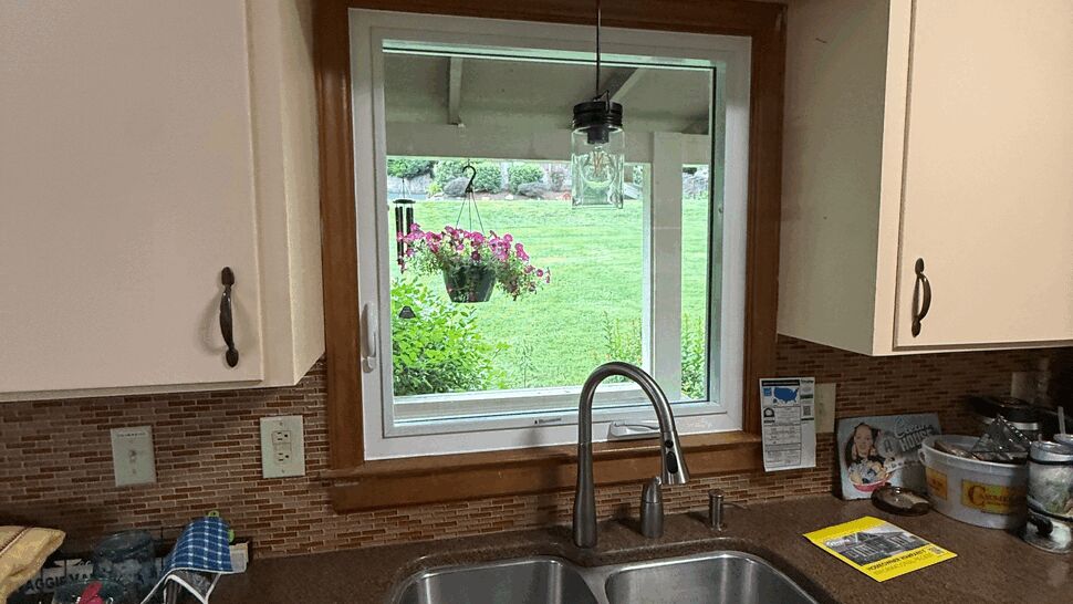 Interior view of a white-framed kitchen sink window overlooking the backyard and hanging planter.