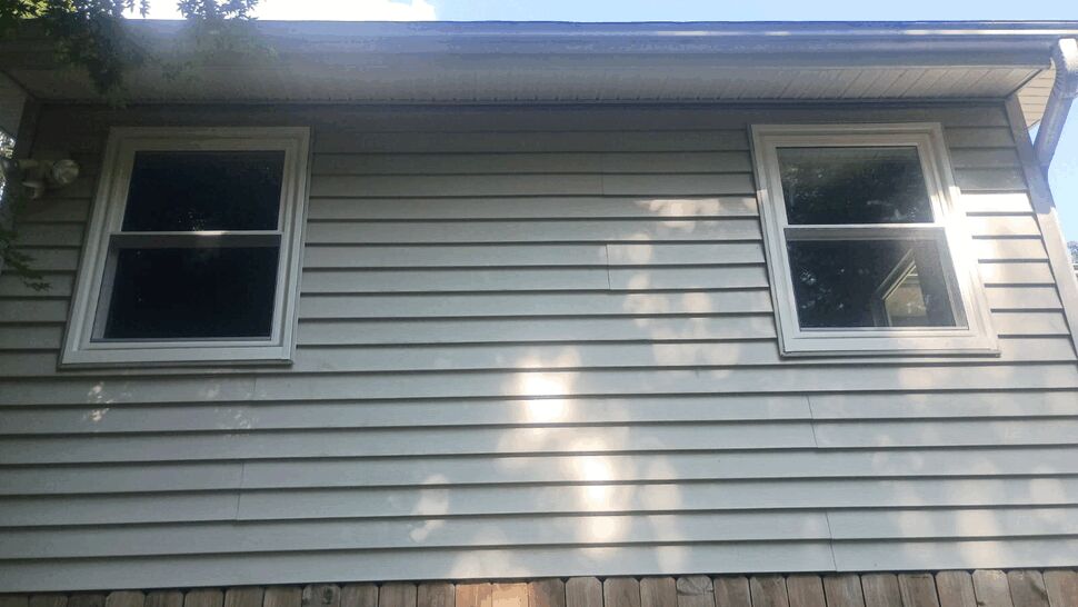 Two upper-story white framed windows on beige siding above a wooden fence