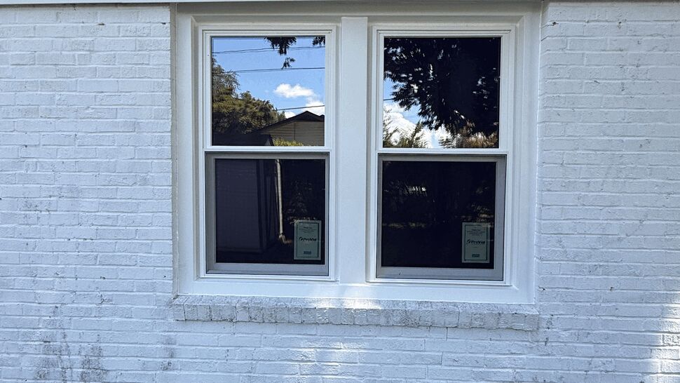 White brick wall with a pair of white double-hung windows reflecting yard