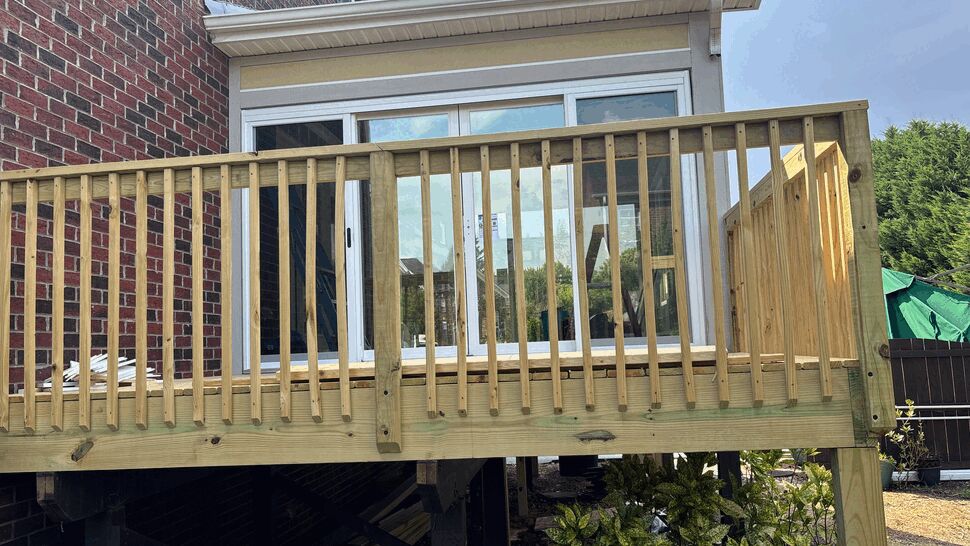 Wooden deck railing in front of sliding glass door on a raised patio