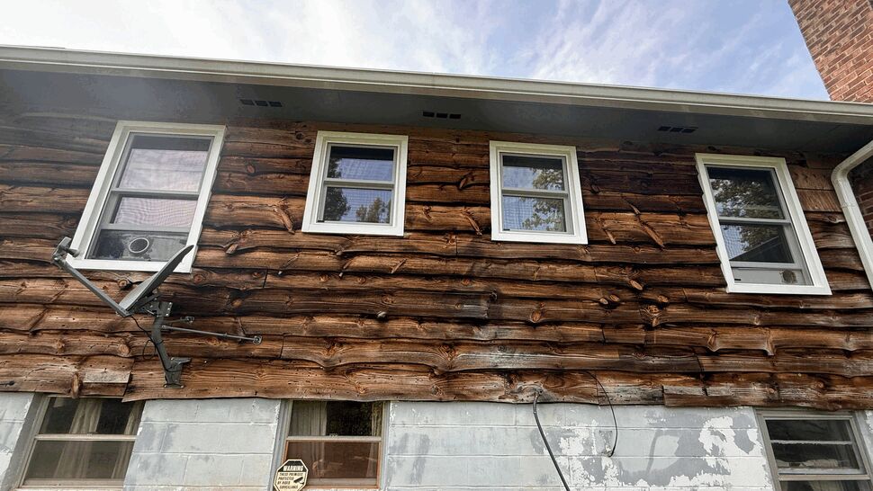 Multiple white-framed upper windows across weathered wood siding with basement vents below