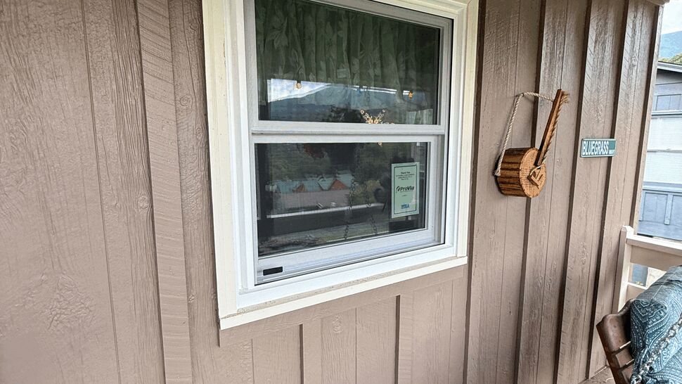 Single-hung white window on porch wall with a hanging basket and wood siding.