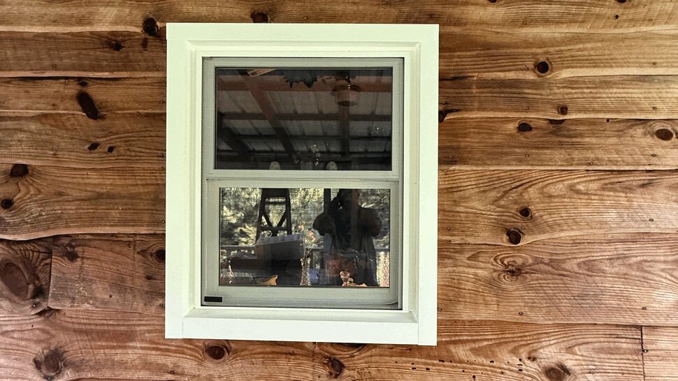Small white-framed window set in rustic cedar siding with porch railing at right