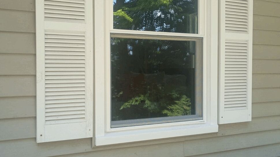 White framed double-hung window with shutters on beige siding