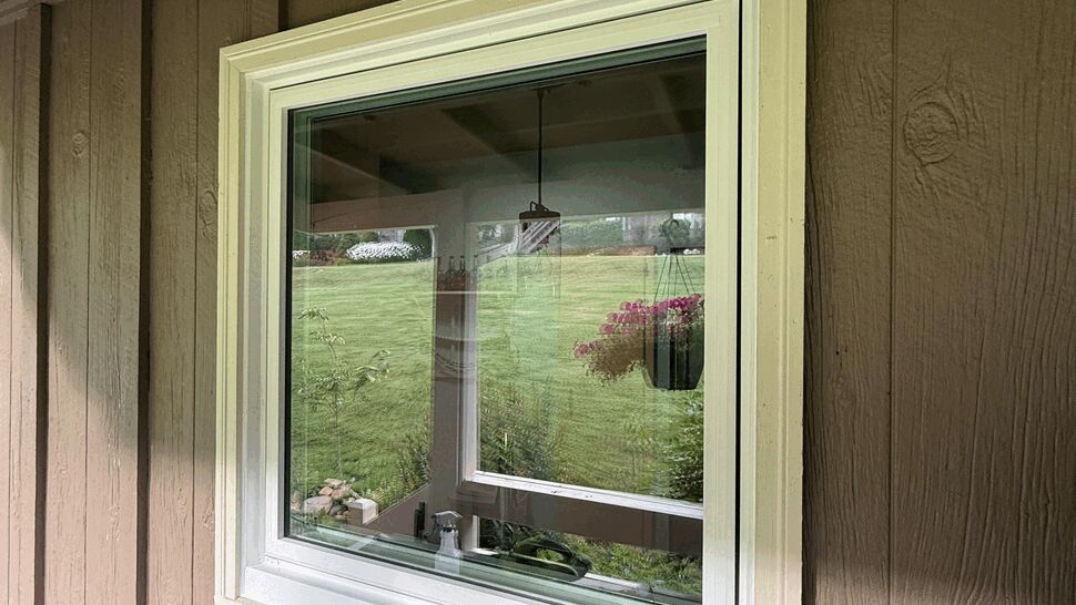 Small square picture window with white trim set in brown board-and-batten siding.