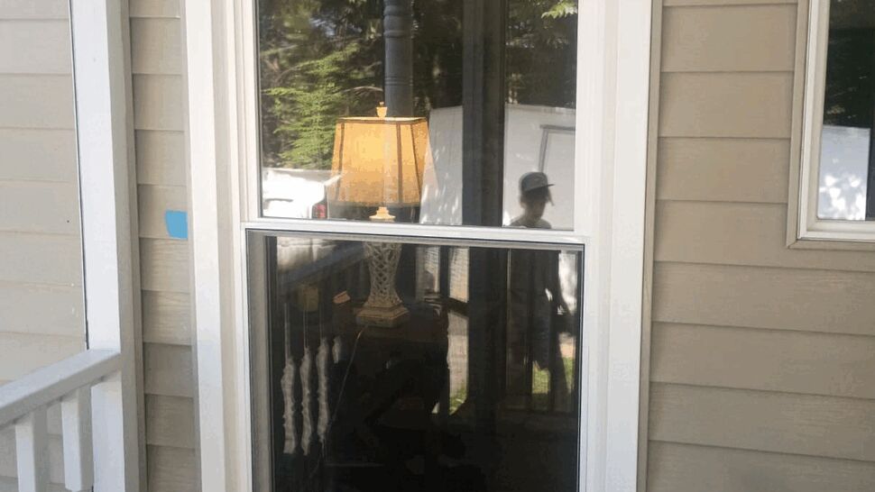 Tall narrow porch window reflecting an interior lamp and railing