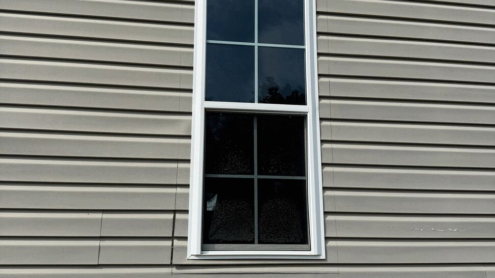 Tall single sash window on beige vinyl siding