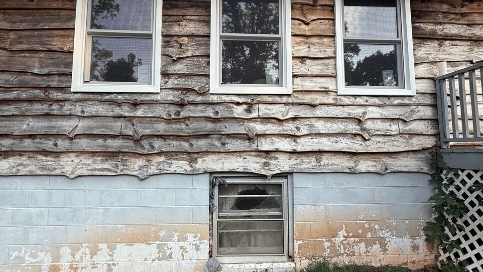 Three white windows in aged wood siding with small basement window below