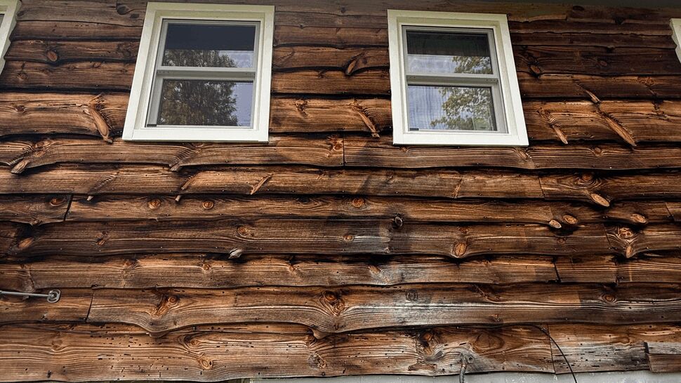 Two upper white windows on log-style wood siding above a painted block foundation