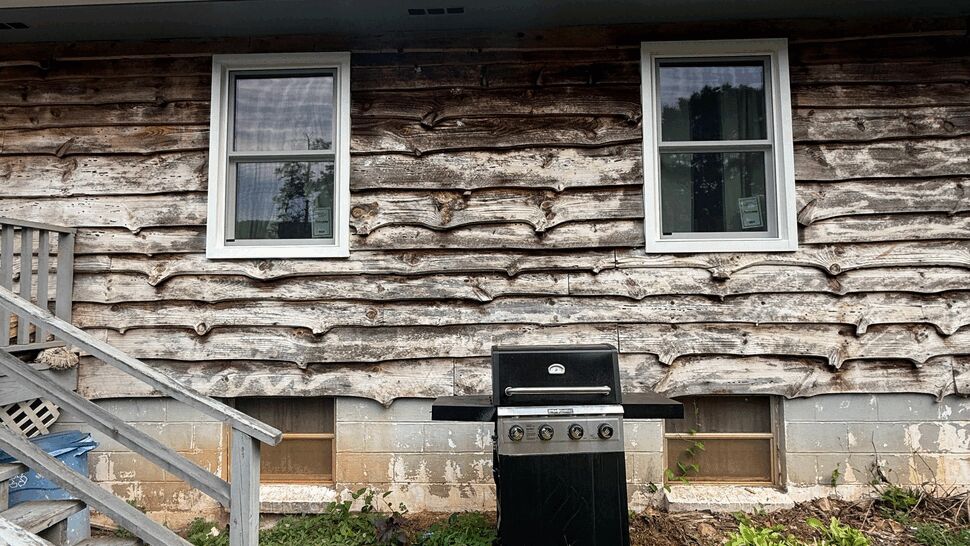 Two white windows above a barbecue grill and grassy yard beside wooden steps