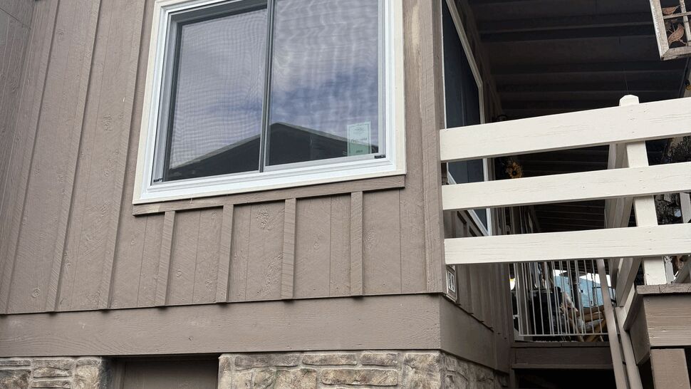 Upper-floor sliding window on brown siding above a stone foundation and exterior stairs.