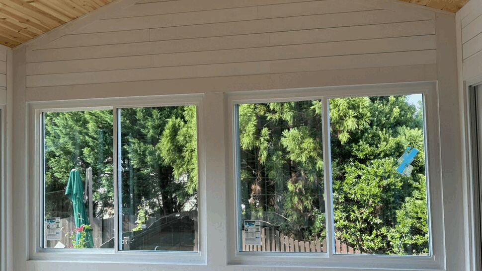 Two large windows under a vaulted wood ceiling looking out to trees
