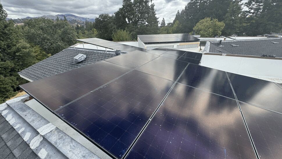 Close-up of reflective black solar panels on a residential roof under cloudy sky.
