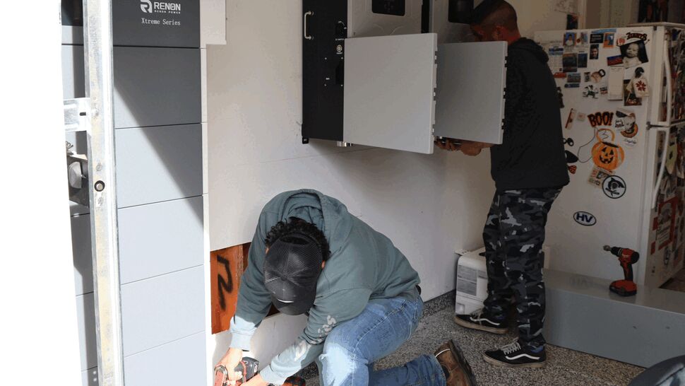 Installers fitting wall-mounted battery modules and inverters inside a garage