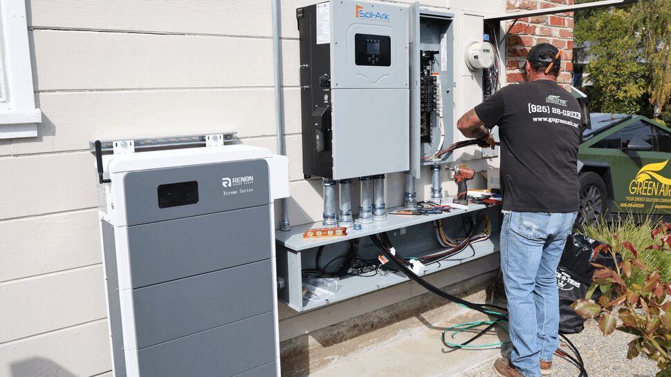 Technician wiring an outdoor inverter and battery connection on a home exterior