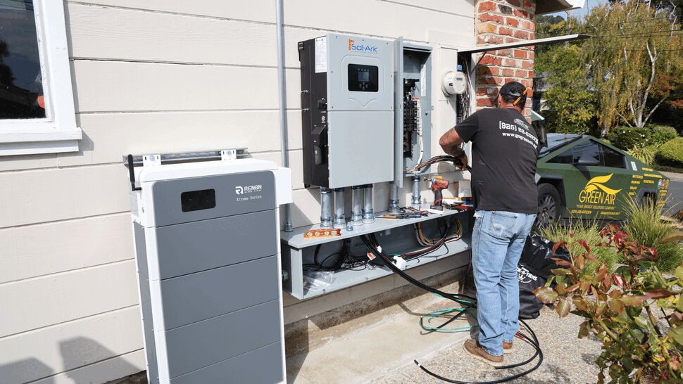 Technician wiring inverter and battery system outdoors next to home