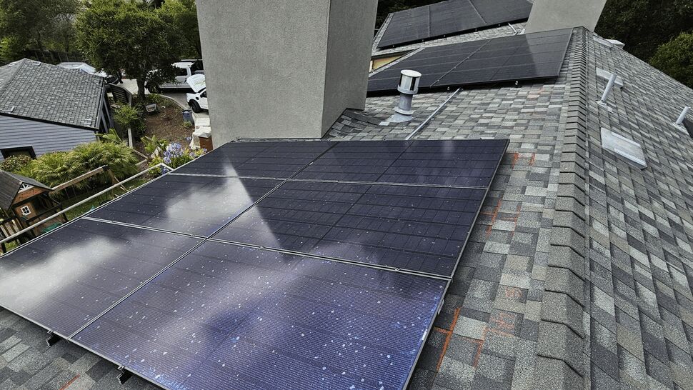 Array of solar panels mounted on an asphalt shingle roof near a chimney