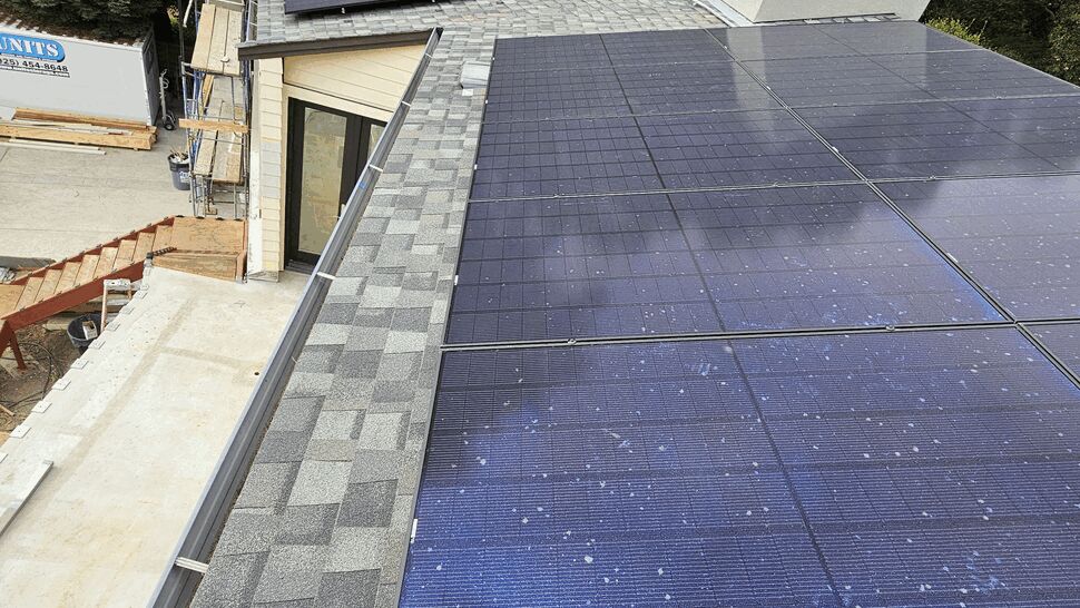 Perspective shot of solar panels along a roofline with surrounding trees