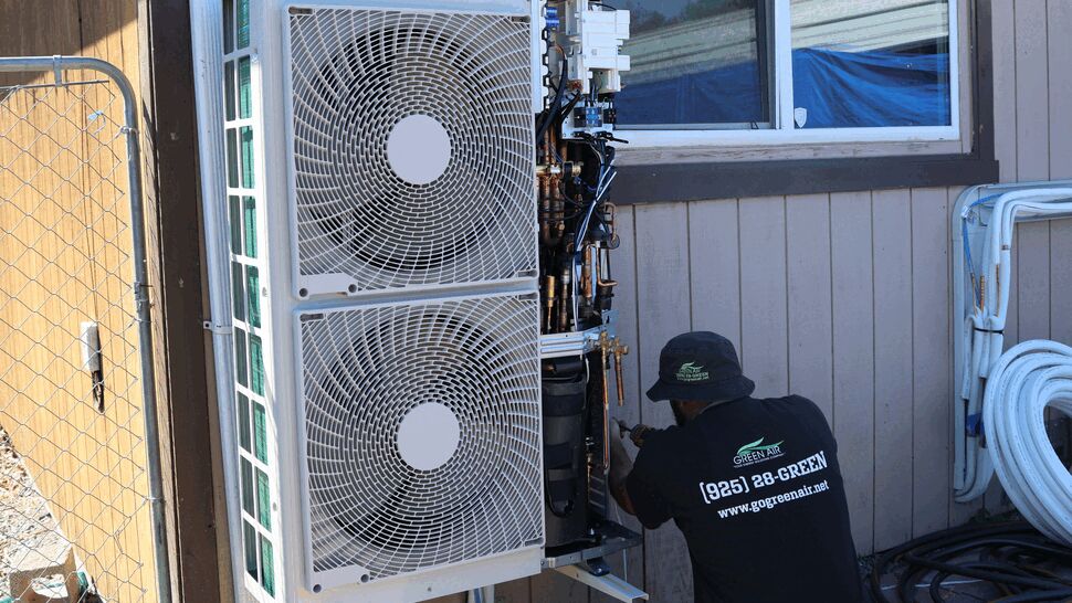 Technician working on an outdoor mini-split condenser mounted on a house exterior