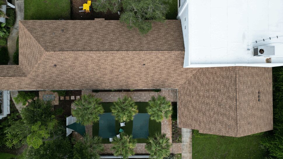 Aerial photo of brown shingle and white flat roofs above a pool and palm trees