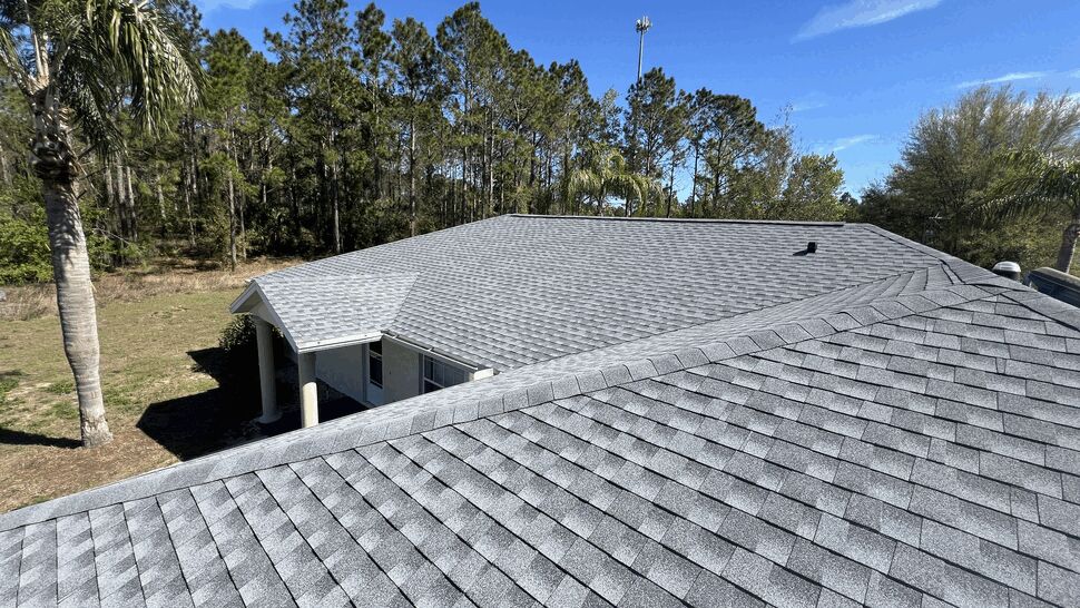 Aerial view of grey asphalt shingle roof on a residential home with trees in background