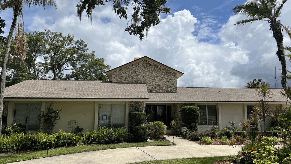 Ranch-style house front with asphalt shingle roof and landscaped yard under partly cloudy sky