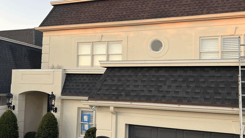 Two-Story Shingle Roof and Gutters | Next Level Roofers Inc Two-story beige house with dark shingle roof accents above garage and white gutters.
