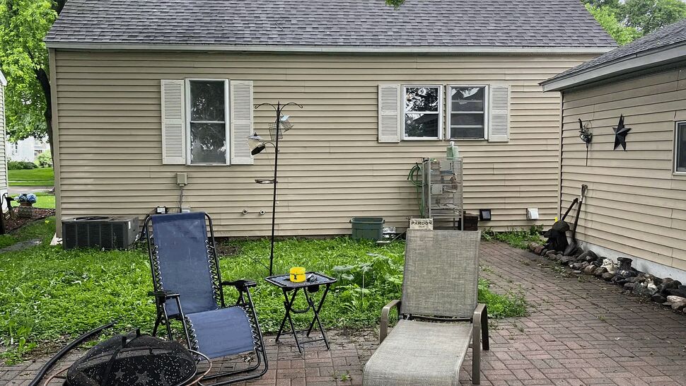 Backyard patio seating and outdoor space | Lutgen Companies Backyard brick patio with lounge chairs, small table and fire pit under tree shade.